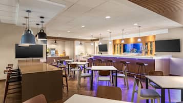 Un restaurante moderno con zona de bar, varias mesas y sillas, y un televisor de pantalla plana grande.