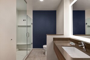 Un baño moderno con cabina de ducha de vidrio, un inodoro blanco y un espejo grande sobre un lavamanos con encimera de madera.