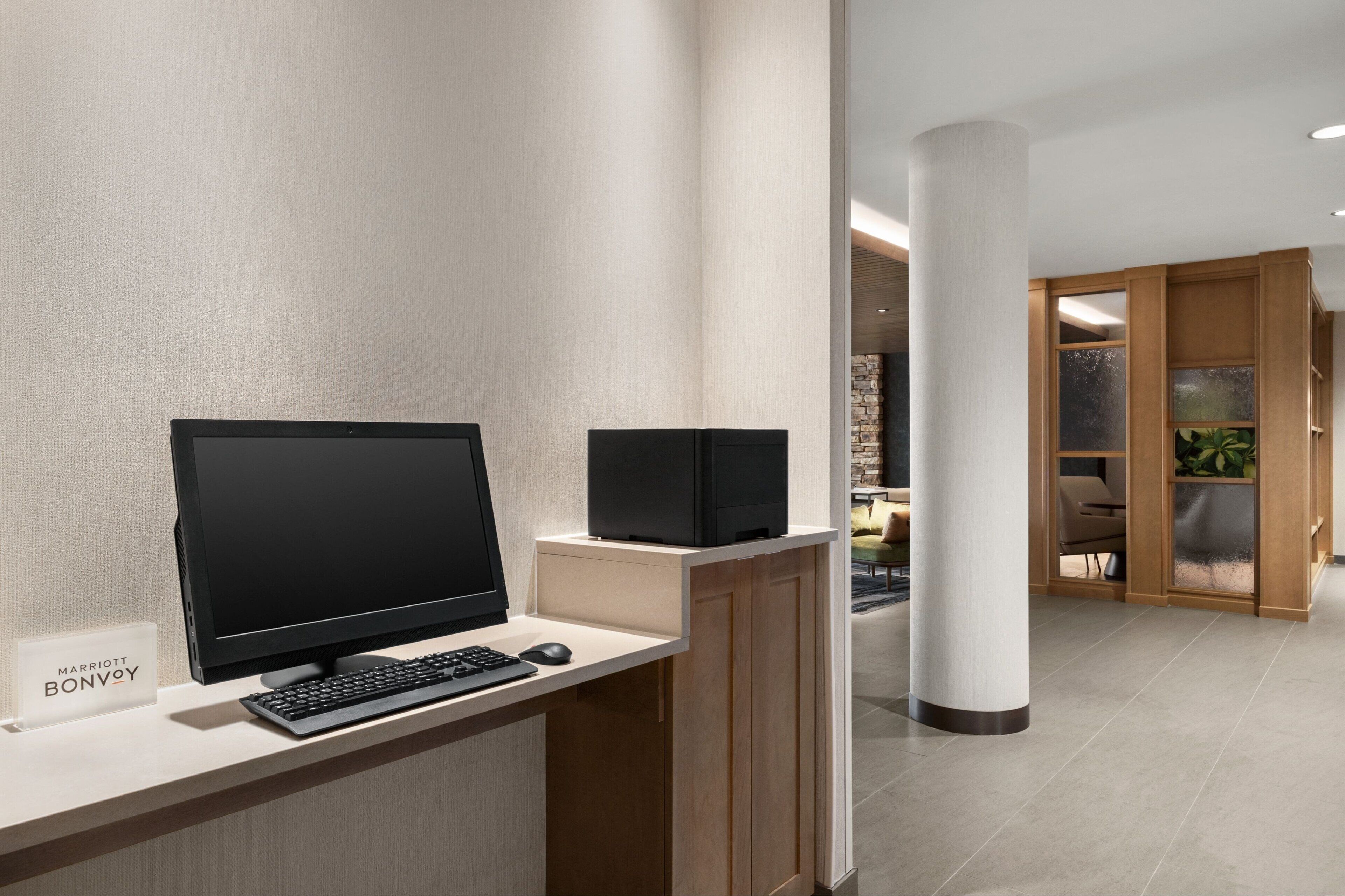 A modern hotel lobby with a reception desk, a flat-screen monitor, a keyboard, and a small sign.