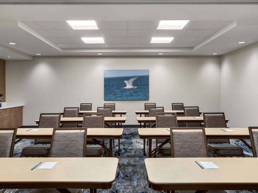 Un salón de conferencias con mesas y sillas dispuestas para reuniones, un cuadro de una gaviota en la pared y una puerta de madera a la derecha.