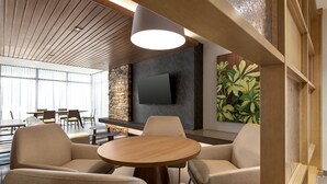 Un área de descanso moderna con una mesa redonda de madera, asientos cómodos, una pared decorativa de piedra y un televisor de pantalla plana.