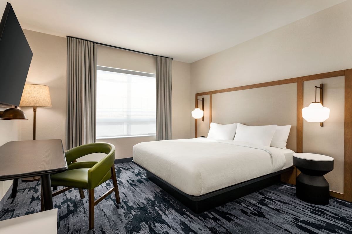 Una habitación de hotel con cama, escritorio, silla, lámpara y mesita de noche.