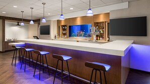 Una zona de bar moderna con una barra larga, taburetes, un gran acuario y una variedad de botellas y vasos.