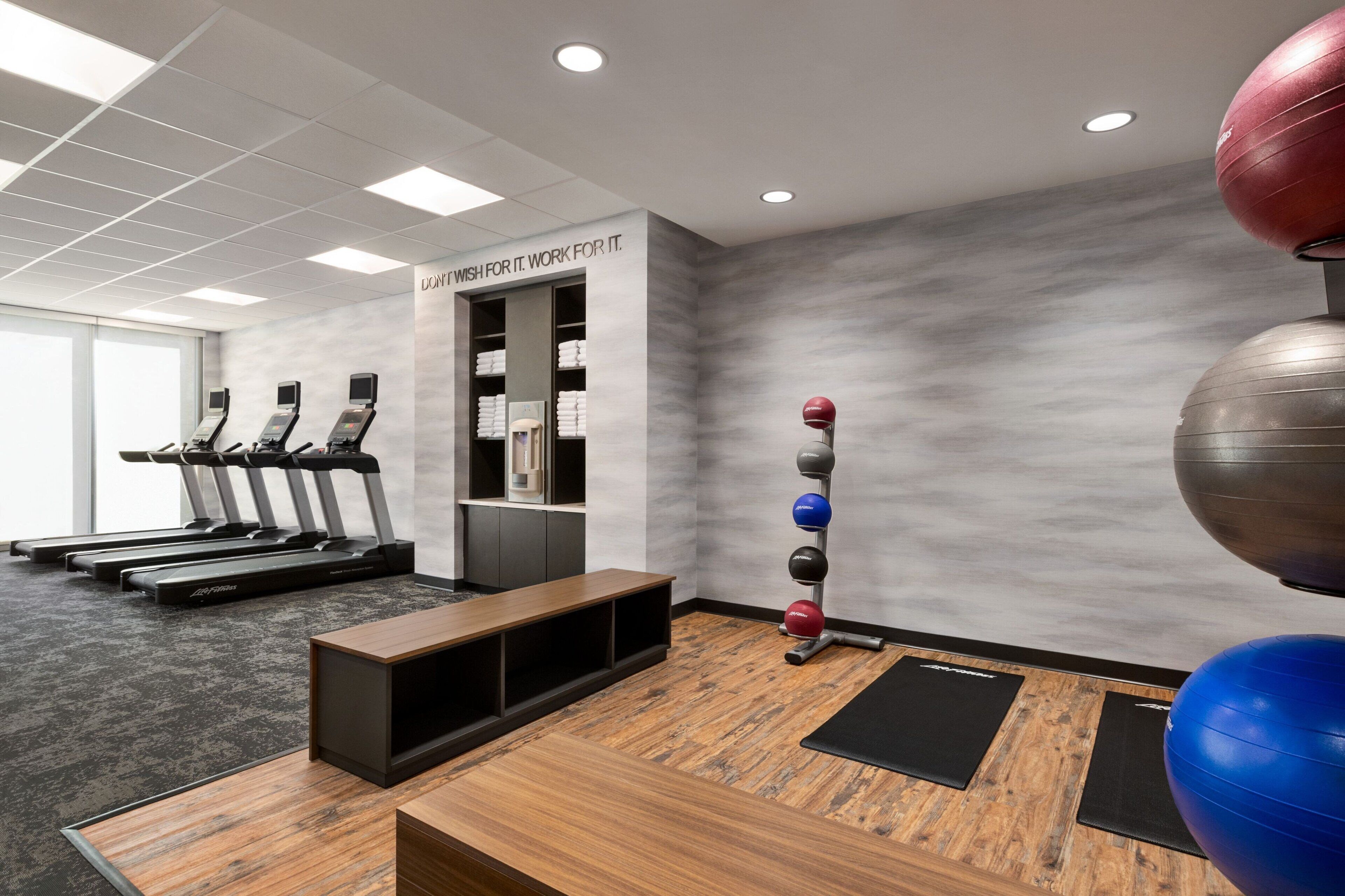 A gym with treadmills, a bench, exercise balls, and a wall with motivational text.
