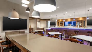 A modern bar area with a long counter, multiple seating options, and pendant lighting.