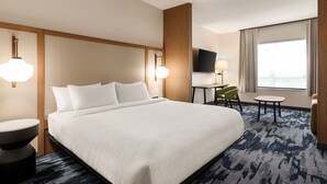 Una habitación de hotel con una cama grande, un escritorio, una silla y un televisor sobre un soporte.