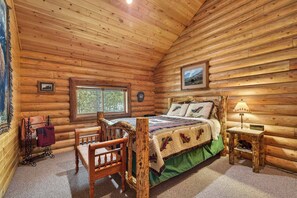 A log cabin bedroom with a bed, a chair, a small table, and a window.
