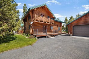 A log cabin with a balcony, a garage, and a driveway.