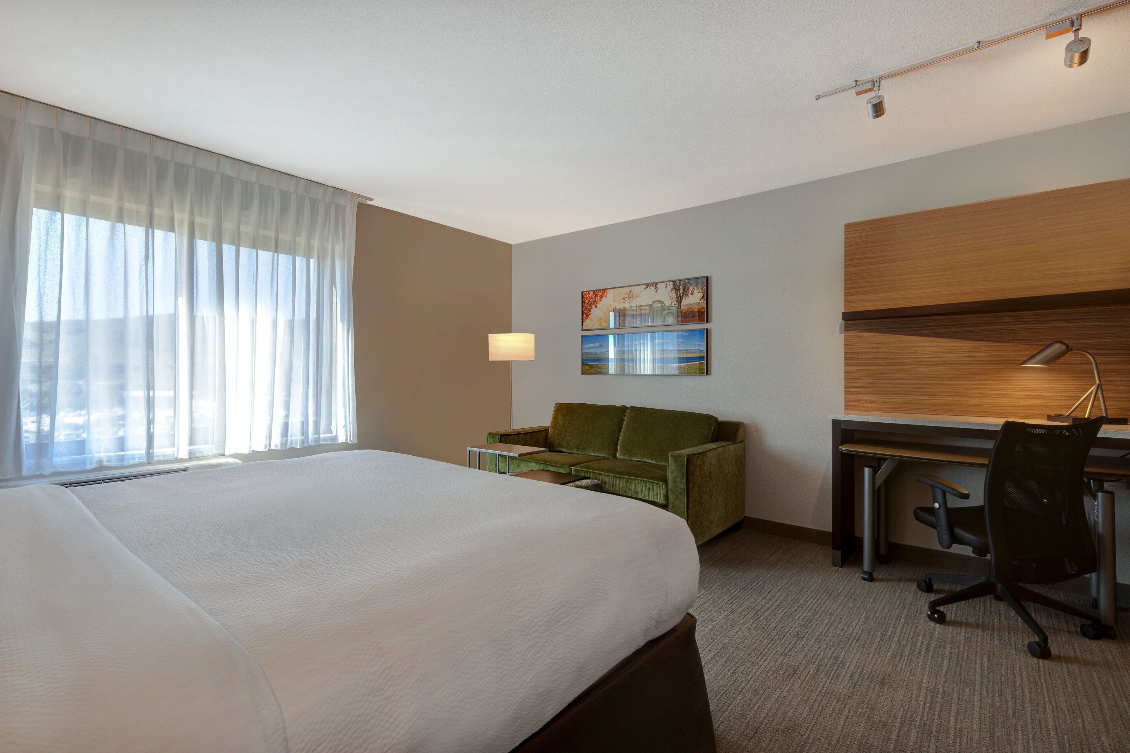 Una habitación de hotel con una cama grande, un escritorio, un sofá verde y un cuadro en la pared.