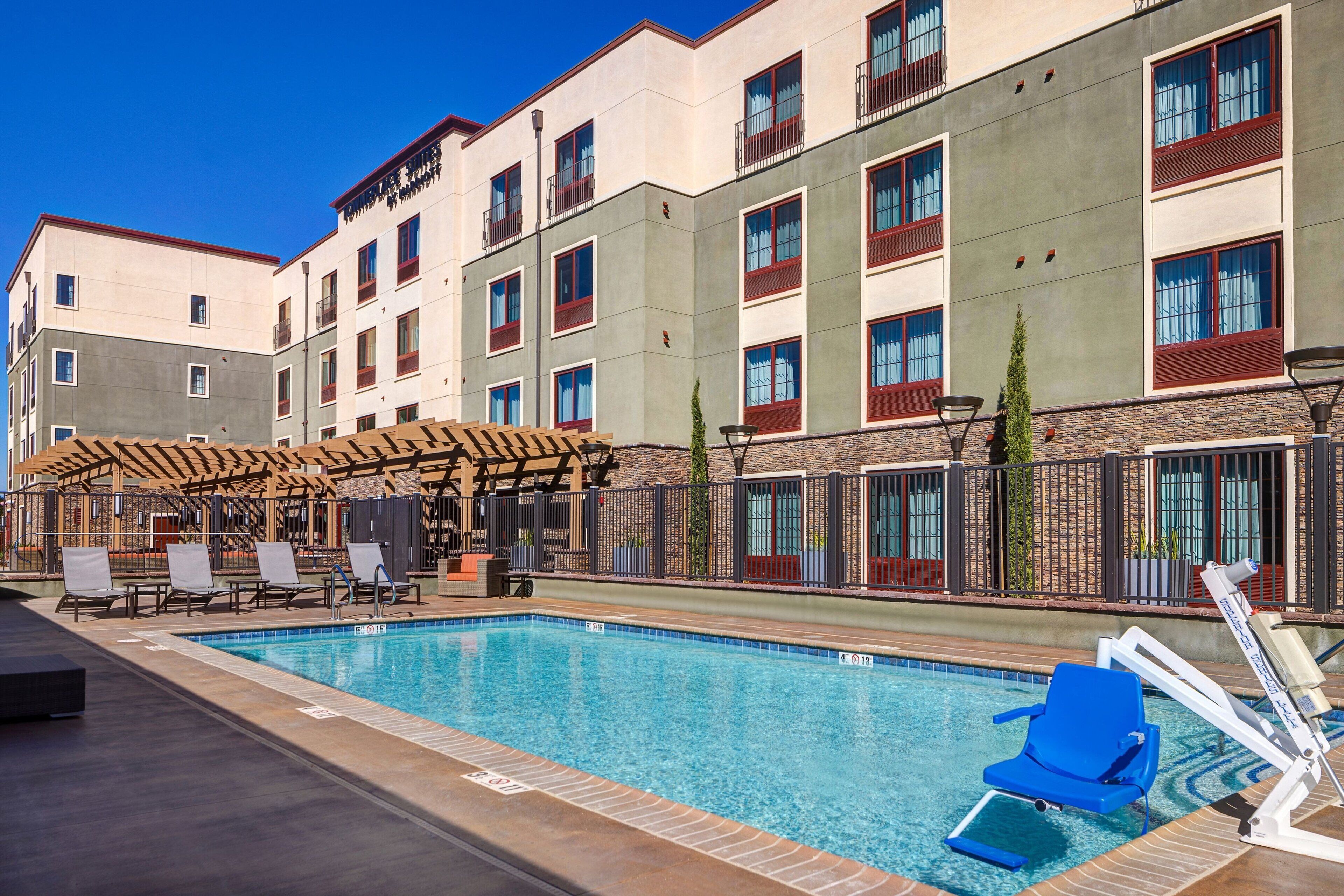 A swimming pool with lounge chairs and a covered seating area, surrounded by a multi-story building with balconies.