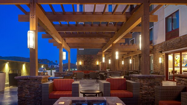 An outdoor patio area with stone walls, wicker furniture, and a stone fire pit. - TownePlace Suites San Luis Obispo (San Luis Obispo)