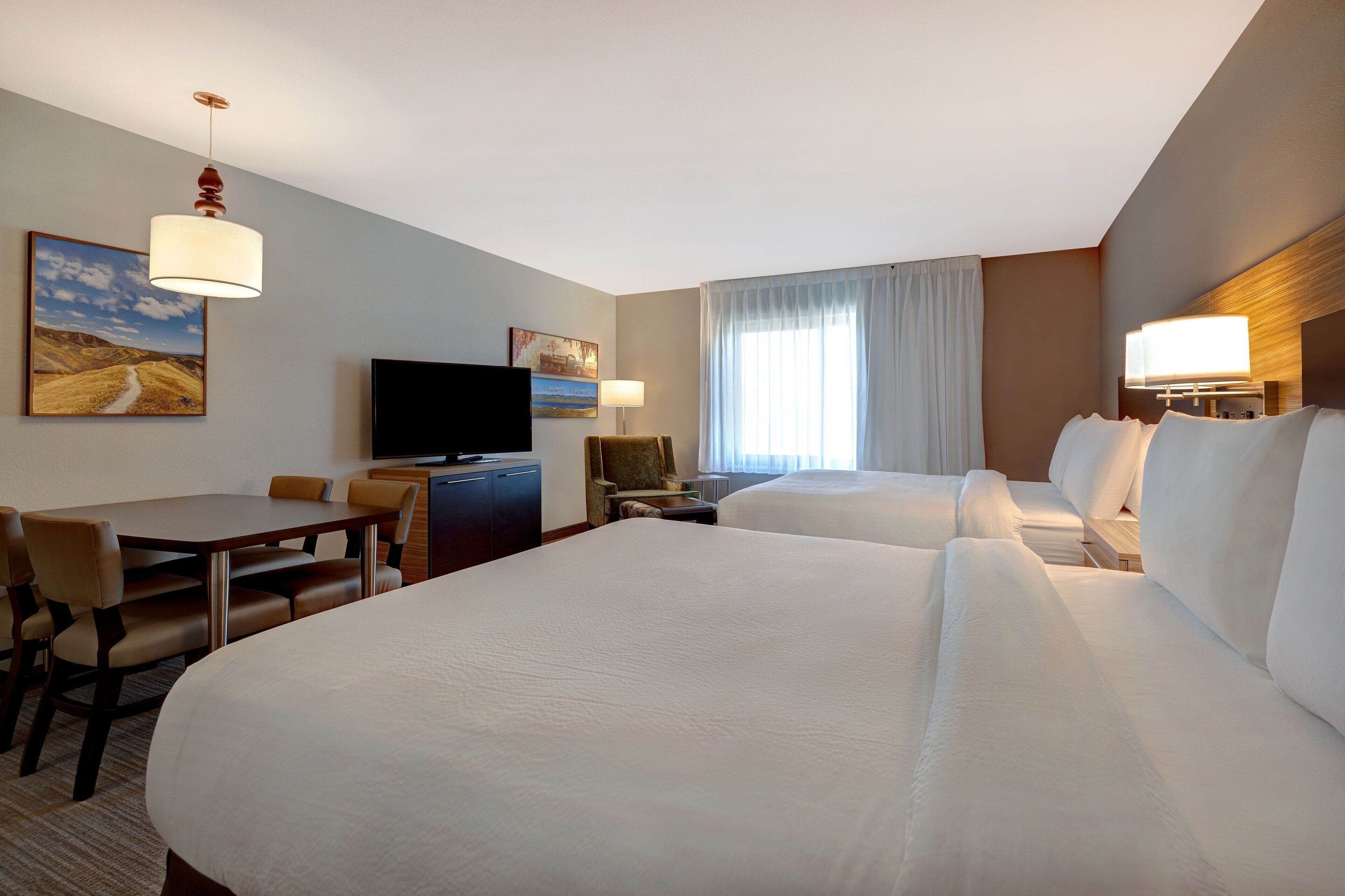 A hotel room with two beds, a desk, a television, and a window with curtains.