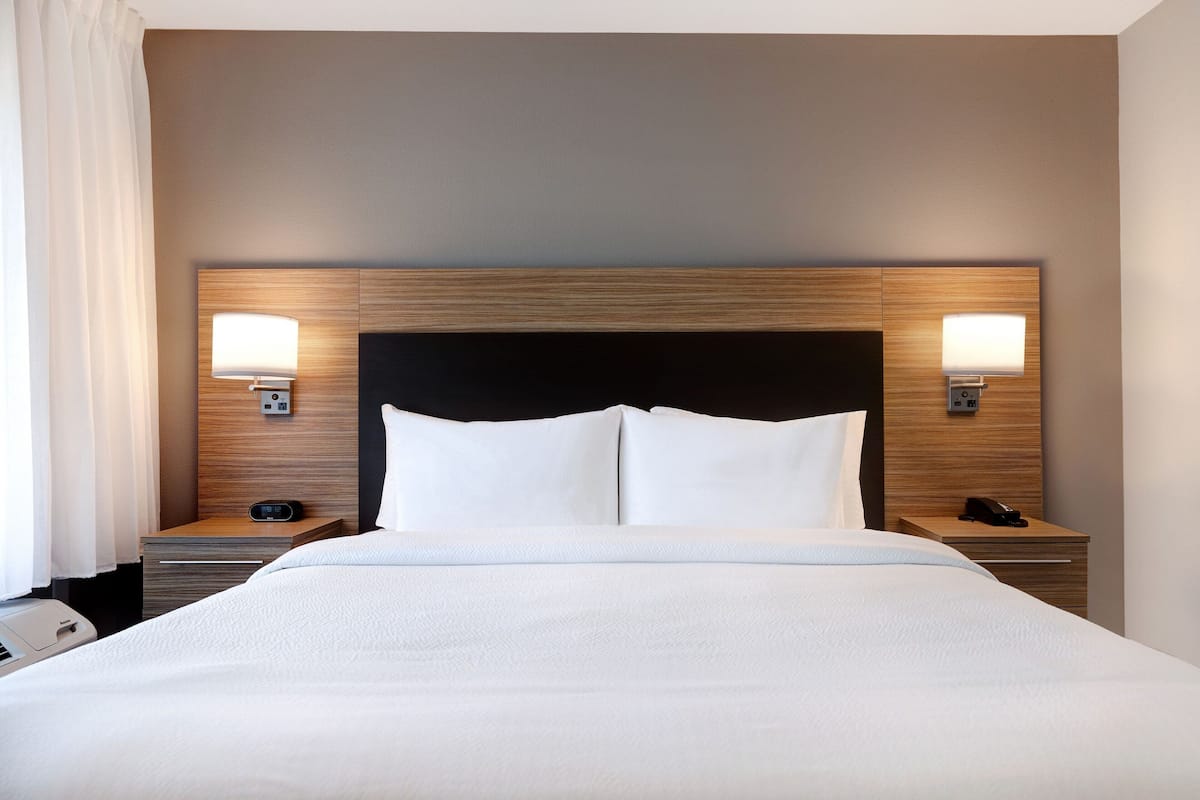Une chambre d’hôtel avec un grand lit, deux tables de chevet avec des lampes et une tête de lit moderne.