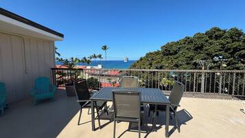 Enjoy the ocean view from this balcony with a table and chairs, surrounded by lush greenery.