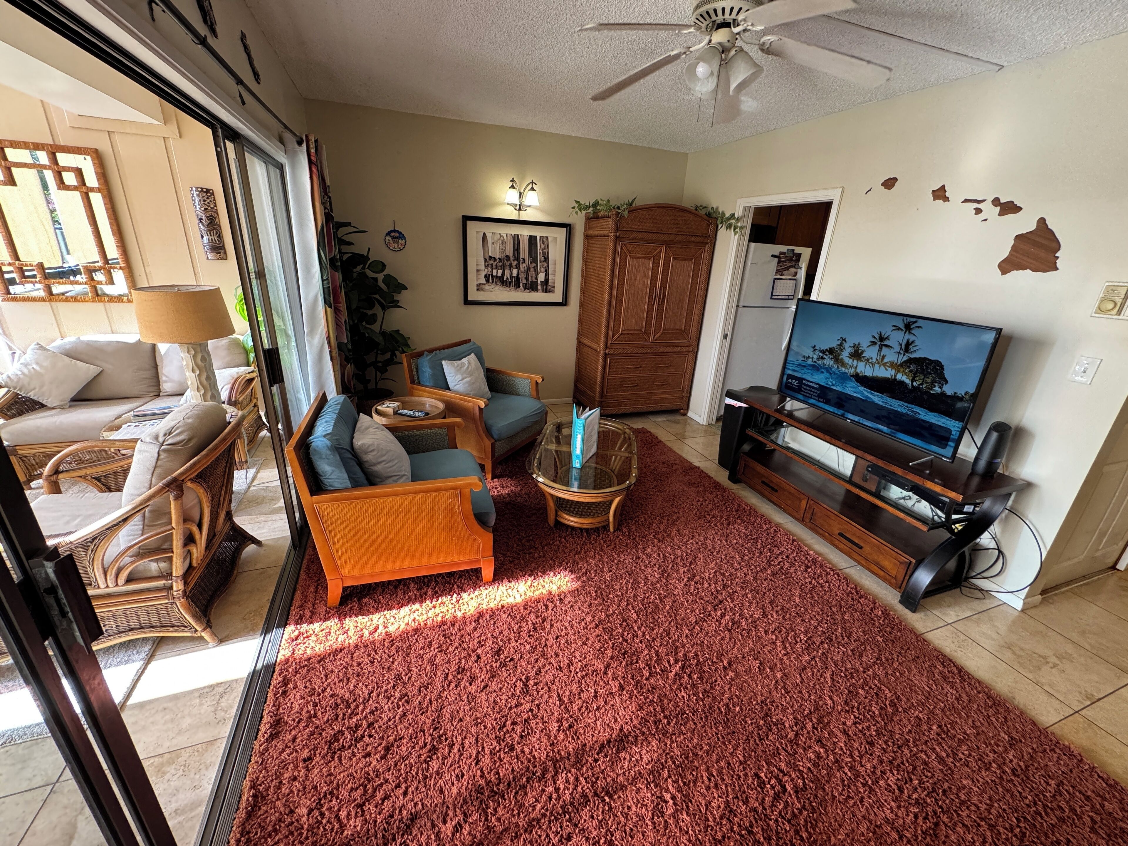 A living room with a red carpet, wicker furniture, a television, and a ceiling fan.