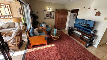 A living room with a red carpet, wicker furniture, a television, and a ceiling fan.