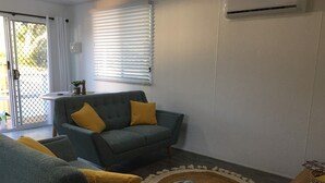 A living room with a grey sofa and armchairs, a round rug, and a wooden side table with a remote control.