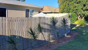 A wooden fence with a number '60' on it, a house with a garage door, and several small plants in front.