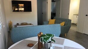 A modern living room with a blue sofa, a white coffee table, and a TV mounted on the wall.