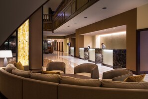 Um hall de hotel com balcão de atendimento, área de estar e escada.