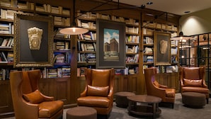 Una biblioteca con sillones de cuero, estanterías y obras de arte enmarcadas.