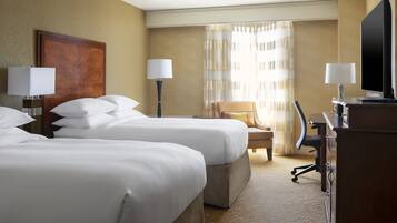 A hotel room with two beds, a desk, a chair, and a television.