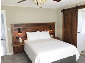 A bedroom with a wooden headboard, two bedside lamps, a bed with white bedding, a nightstand, and a sliding barn-style door. - Fully Renovated Home on a Working Farmstead (Powell)