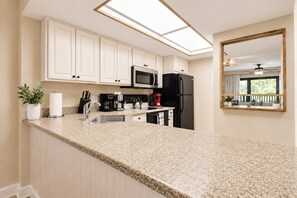 A kitchen with white cabinets, a black refrigerator, a microwave, a kettle, and a coffee maker. - Park Shore Resort-Top Floor BLDG J #455-Great View (Park Shore Resort)