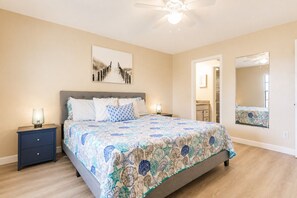 A bedroom with a bed, nightstands, a ceiling fan, a large mirror, and a door leading to a bathroom. - Park Shore Resort-Top Floor BLDG J #455-Great View (Park Shore Resort)