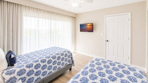 Une chambre d’hôtel avec deux lits, un ventilateur de plafond, une porte et un tableau au mur.