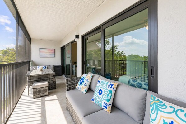 A balcony with a sofa, a table, and chairs, and a view of the outdoors.