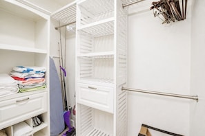 Ein weißer Kleiderschrank mit Regalen, einem Stapel gefalteter Handtücher und einem Staubsauger.