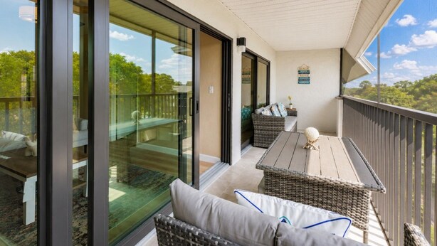 Un balcon avec une porte vitrée, des meubles en osier et une vue sur l’extérieur.