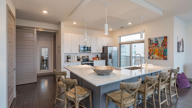 A modern kitchen with white cabinets, stainless steel appliances, and a large island with bar stools. - Chic 2BR Condo w/ Open Living Space | Sleeps 4! (Nashville)