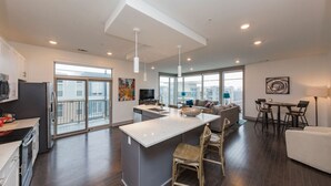 A modern kitchen with a central island, a dining area with a table and chairs, and a living area with a sofa and a TV. - Chic 2BR Condo w/ Open Living Space | Sleeps 4! (Nashville)