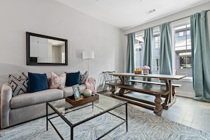 Relax in this stylish living room with a sofa, coffee table, and dining table, surrounded by large windows and a mirror.
