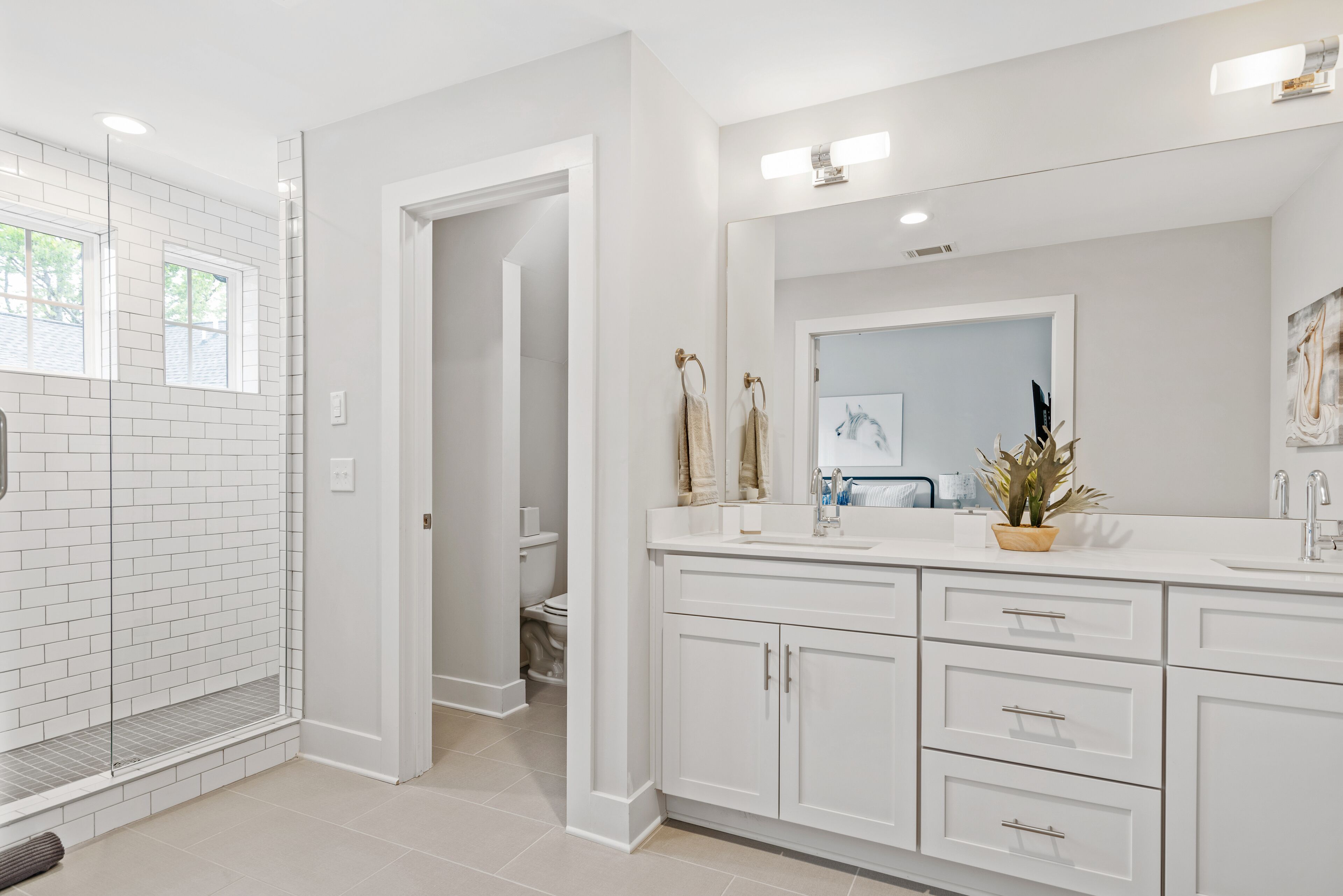 Een moderne badkamer met witte tegels, een douche, een grote spiegel en een wastafel met kastjes.