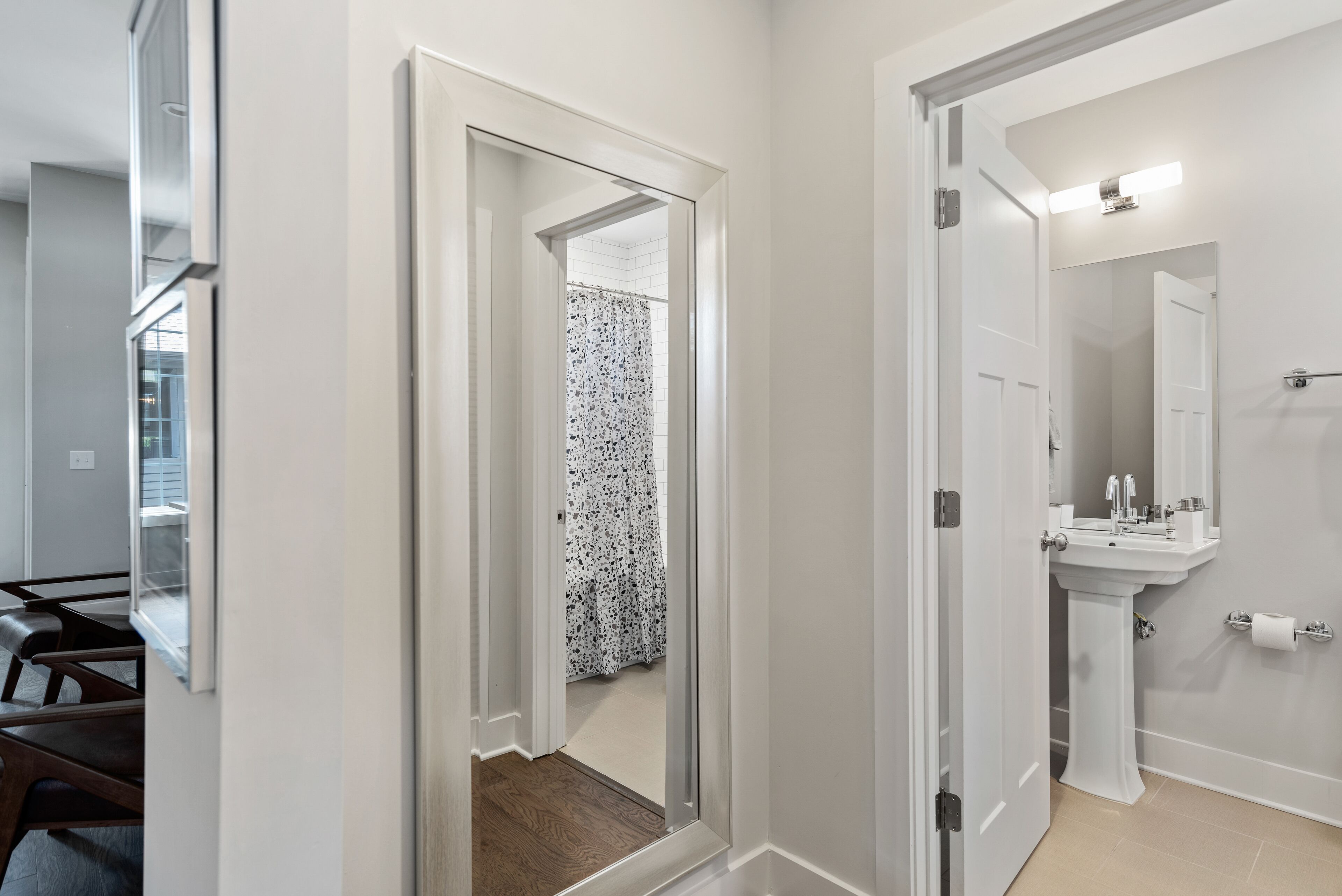 Un pasillo con una puerta que da a un baño con lavamanos y espejo.