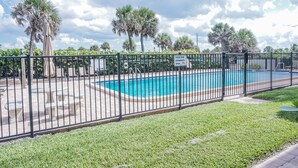 A rectangular swimming pool surrounded by a black metal fence, with a grassy area in the foreground and palm trees in the background. - Casa al Mare – Premier "True Beachfront" Living in Vero Beach!  Steps to sand! (Vero Beach)