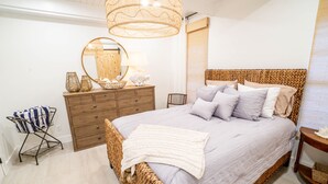 A bedroom with a wicker bed, a wooden dresser, a mirror, and a hanging light fixture. - Casa al Mare – Premier "True Beachfront" Living in Vero Beach!  Steps to sand! (Vero Beach)