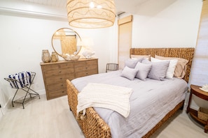 Un dormitorio con una cama de mimbre, un aparador de madera, un espejo y una lámpara colgante.