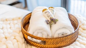 A white towel with a small purple flower and a bottle of coconut milk conditioner placed on a white textured blanket. - Casa al Mare – Premier "True Beachfront" Living in Vero Beach!  Steps to sand! (Vero Beach)