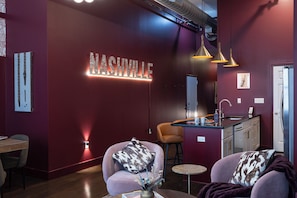En modern inredning med en röd vägg, en neonskylt med texten ”Nashville”, ett köksområde och sittplatser med mönstrade kuddar.