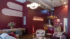 A modern living room with a dining area, a kitchen, and a red accent wall. - Dazzling Downtown Loft in the Heart of Music City (Nashville)