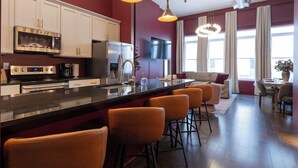 A modern kitchen with white cabinets, a black countertop, and orange bar stools. - Dazzling Downtown Loft in the Heart of Music City (Nashville)
