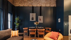 Una sala de estar moderna con techo de ladrillo, paredes oscuras, una mesa de comedor con sillas, un sofá y una pequeña mesa de centro con libros.