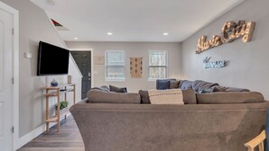 Ein modernes Wohnzimmer mit einem grauen Sofa, einem an der Wand montierten Flachbildfernseher und einem Schild mit der Aufschrift "Music City".
