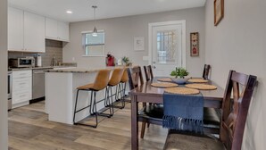 A modern kitchen with white cabinets, a central island, and a dining area with a wooden table and chairs. - Honky Tonk Hideaway on Music Row (Nashville)