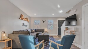 Una sala de estar moderna con un sofá, dos sillones azules, una mesa de centro y un televisor montado en la pared.