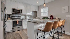 Una cocina moderna con armarios blancos, electrodomésticos de acero inoxidable, una isla grande con taburetes de bar y una lámpara colgante.
